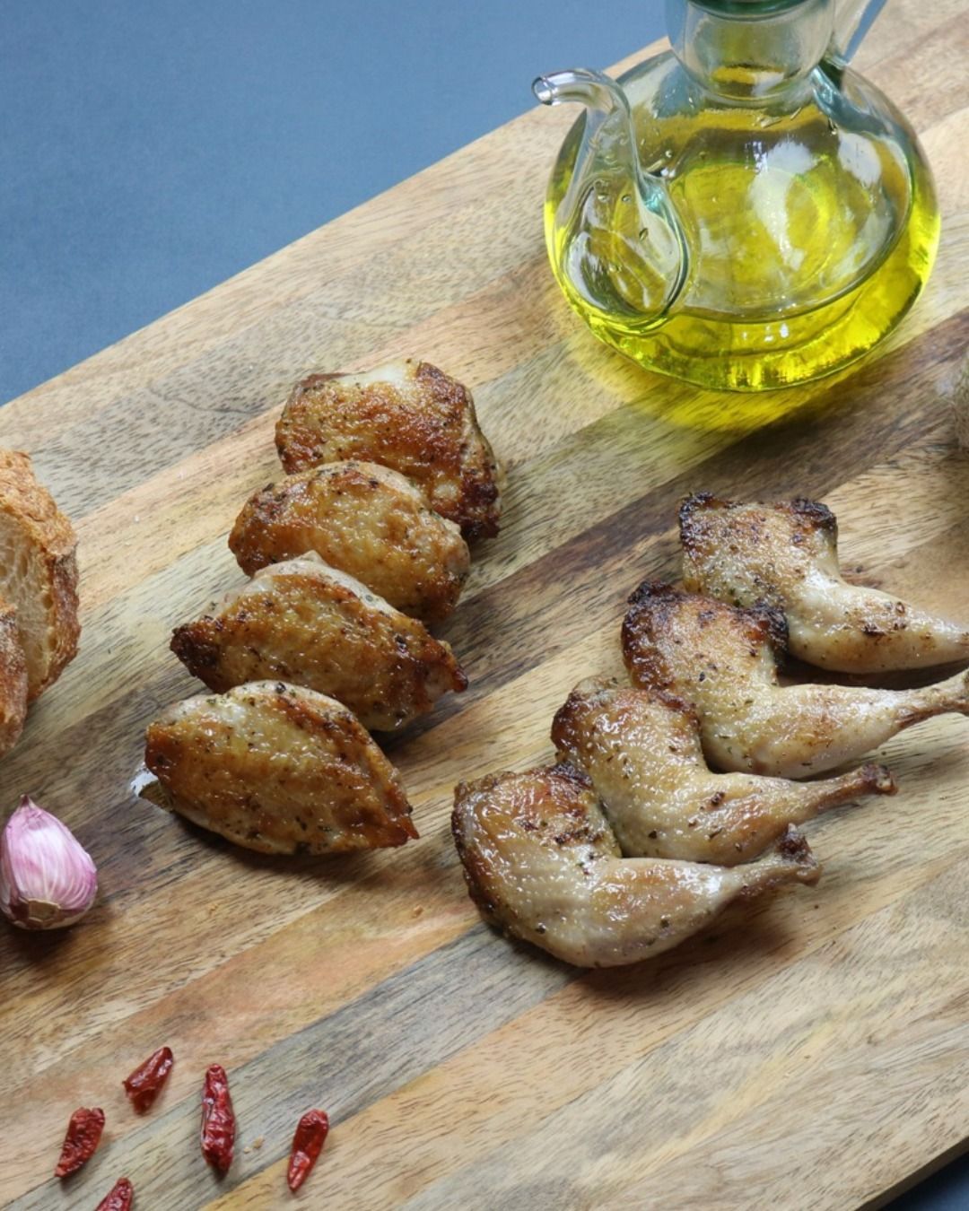 Pan-seared quail breasts and legs on a wooden board with olive oil