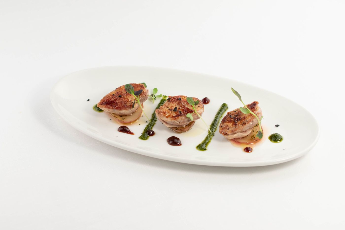 Seared quail breasts with herb oil on an oval plate