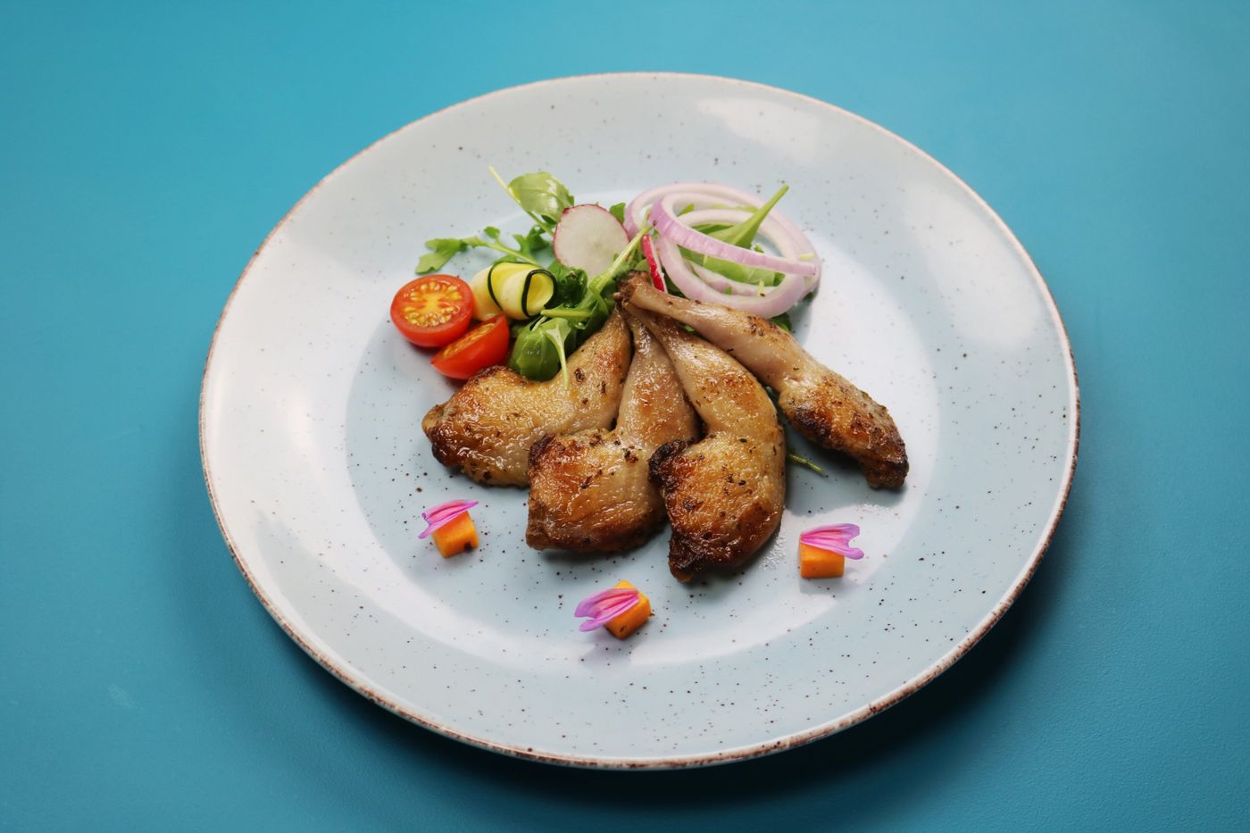 Roasted quail legs with fresh salad on a speckled plate